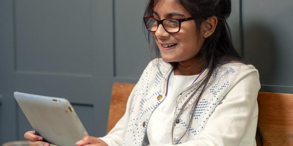 Teenage girl look at iPad in hand, sat in a classroom