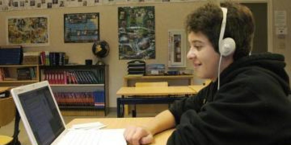 student with headphones , sat at a desk looking at their laptop