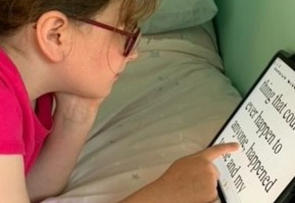 Young girls , head and shoulders view, lying on a bed reading on an iPad in large print