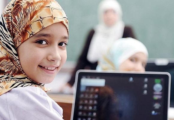 Smiling girl in headress in a classroon an laptop on the desk in front of her